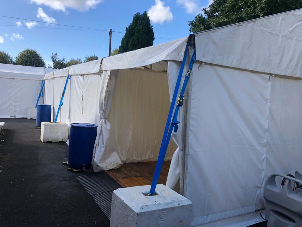 Kilmarnock - The Wards COVID vaccination Clinic Marquee with a wall pulled back for entry to the marquee. The marquee is secured with concrete blocks and water ballast barrels