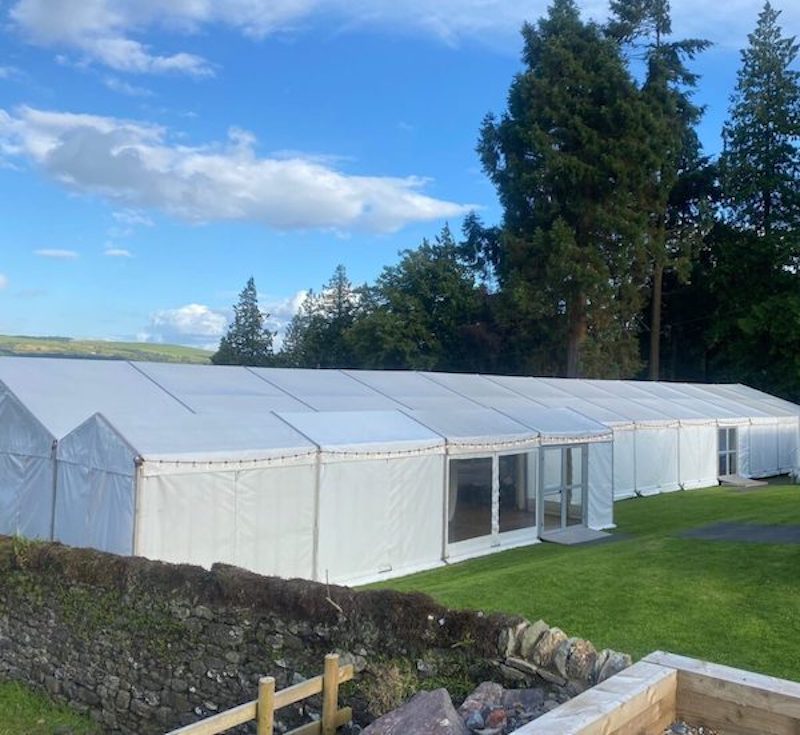 Marquee in private garden in Argyll on bright day with trees, grass, blue sky and clouds.